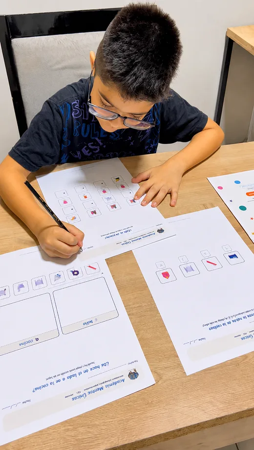 Niño concentrado completando con lápiz una ficha impresa de secuencias sobre la mesa